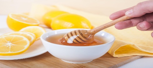 honey in a white ceramic bowl with honey dipper and lemon on a wooden kitchen boar